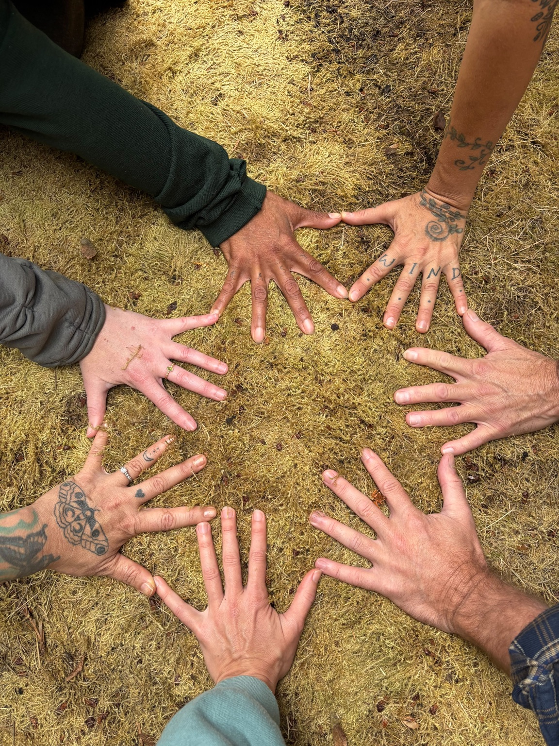 Community members placing their hands in a circle on the earth